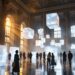 Visitors explore a grand hall with suspended glowing frosted cubes as light sculpture fills the space.