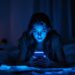 Woman lying on a bed in a dim room, blue light from her smartphone illuminating her face as she looks at the screen.