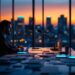 Man in a suit working on a laptop at a conference table by floor-to-ceiling windows at sunset, city skyline in the background.
