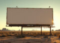 An empty, weathered billboard on rusted metal supports in a desert at sunset with distant mesas on the horizon.